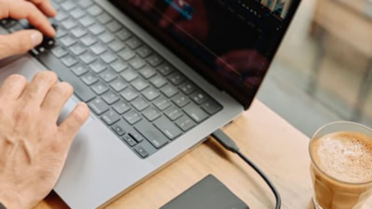 دست بر روی لپ‌تاپ و قهوه در جلو.